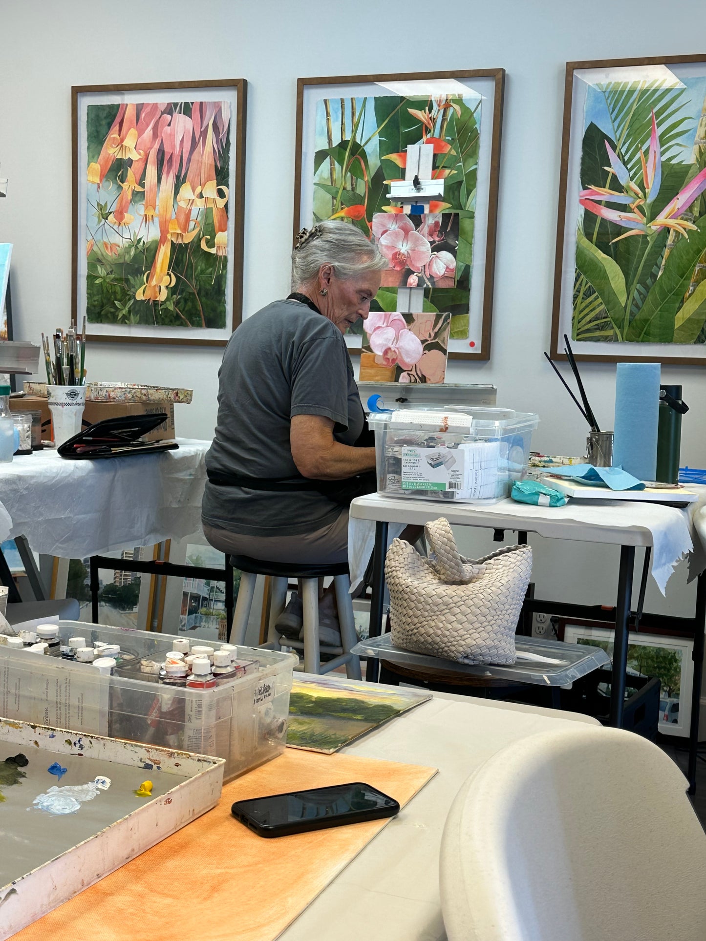 Person working at a table with art supplies and framed artwork in the background