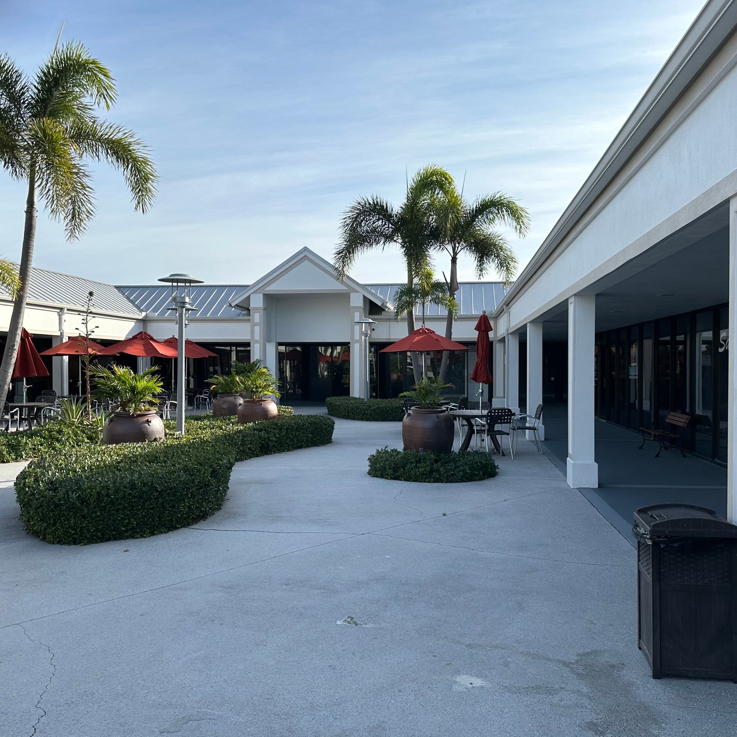Outdoor area with palm trees, tables, and chairs in front of a building.