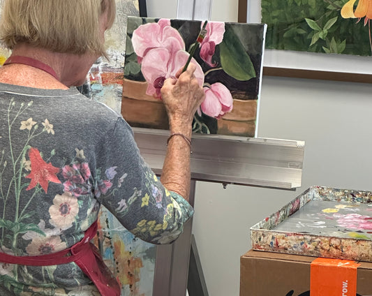 Woman painting an orchid with a paint palette on her right