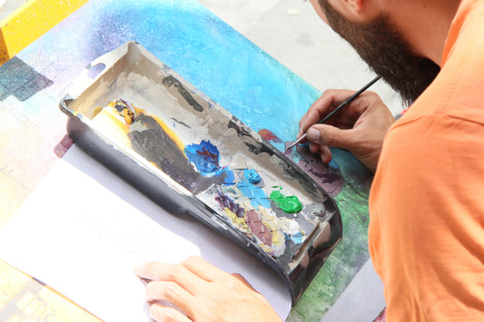 Man wearing an orange shirt painting an abstract image with a painting palette in front of him